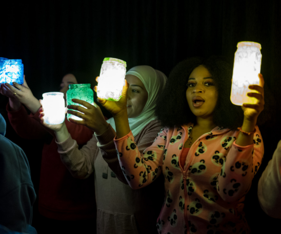 In der Dunkelheit halten mehrere Personen große Teelichter hoch und singen.