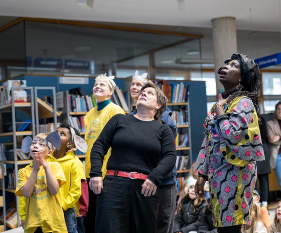 Mehrere bunt gekleidete Personen unterschiedlichen Alters schauen ausdrucksstark nach oben.